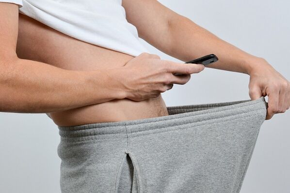 Ein Mann blickt unter seiner Hose auf einen vergrößerten Penis